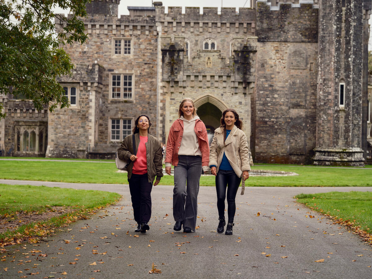 The ladies walk towards the camera with a large castle with intricate architectural designs towers over them in the background