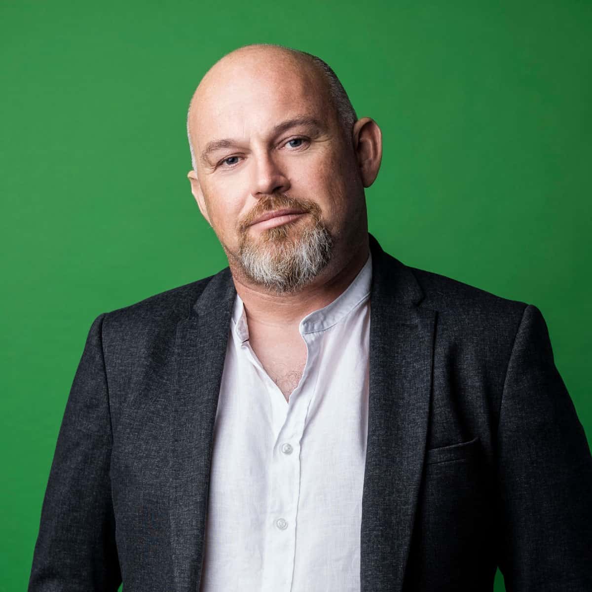 Headshot of CEO & founder of Scurri, Rory O'Connor on a green background to match the Scurri brand colours. He has a neutral expression on his face and is wearing a white shirt and black blazer