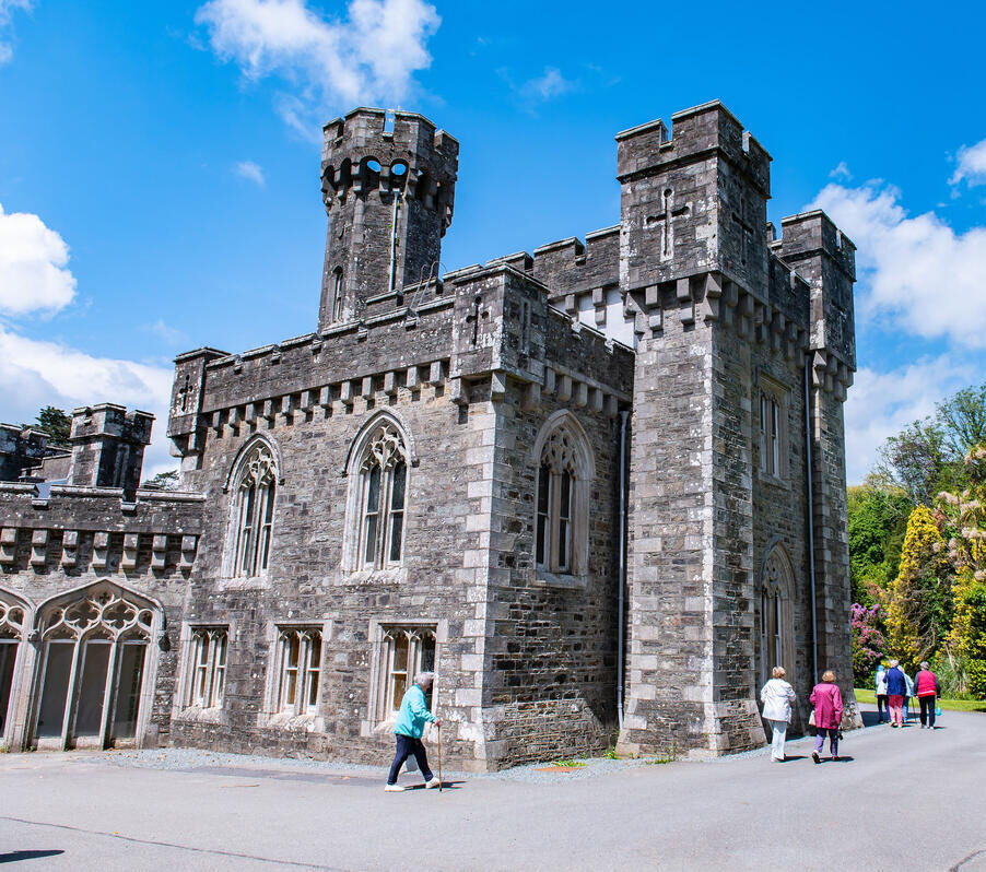 A large stone castle with intricate architectural battlements with people walking around the perimeter.