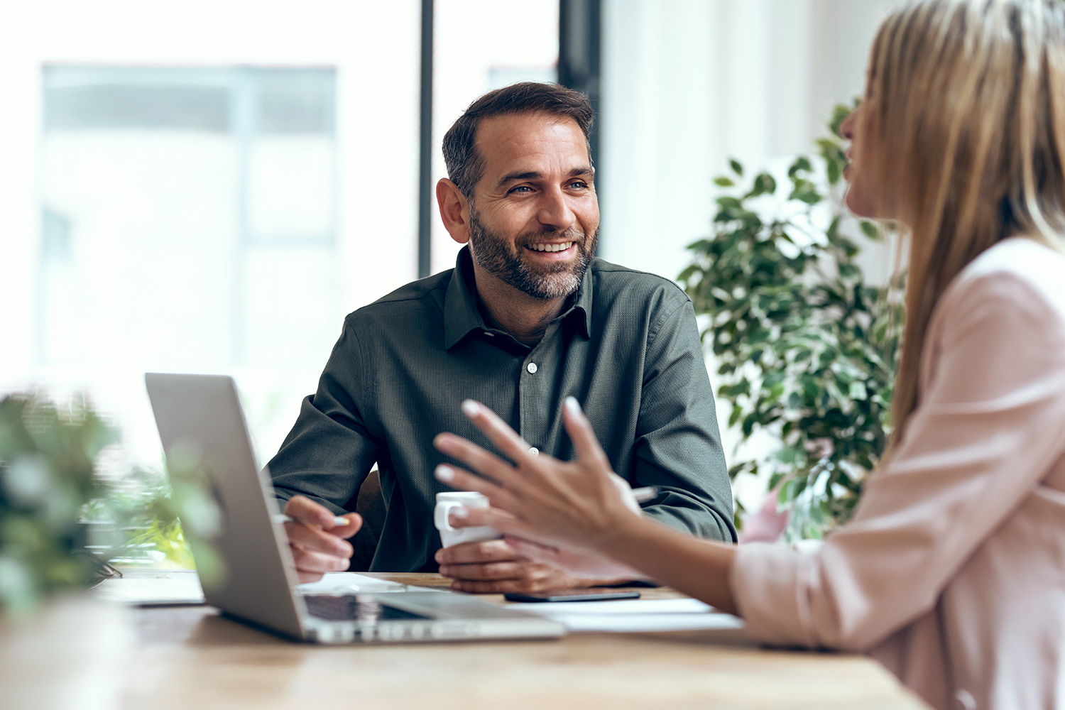 A man and a woman having a meeting, both appear cheery and there is a laptop between the two of them on the tablet
