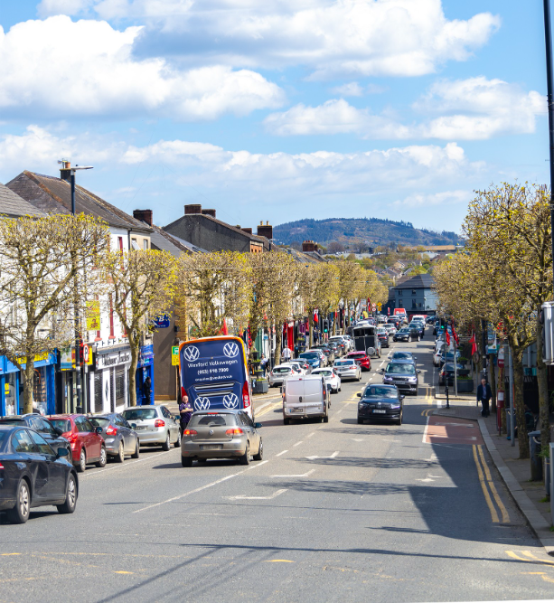 A view down Gorey main street of cars driving with trees lining both sides of the road