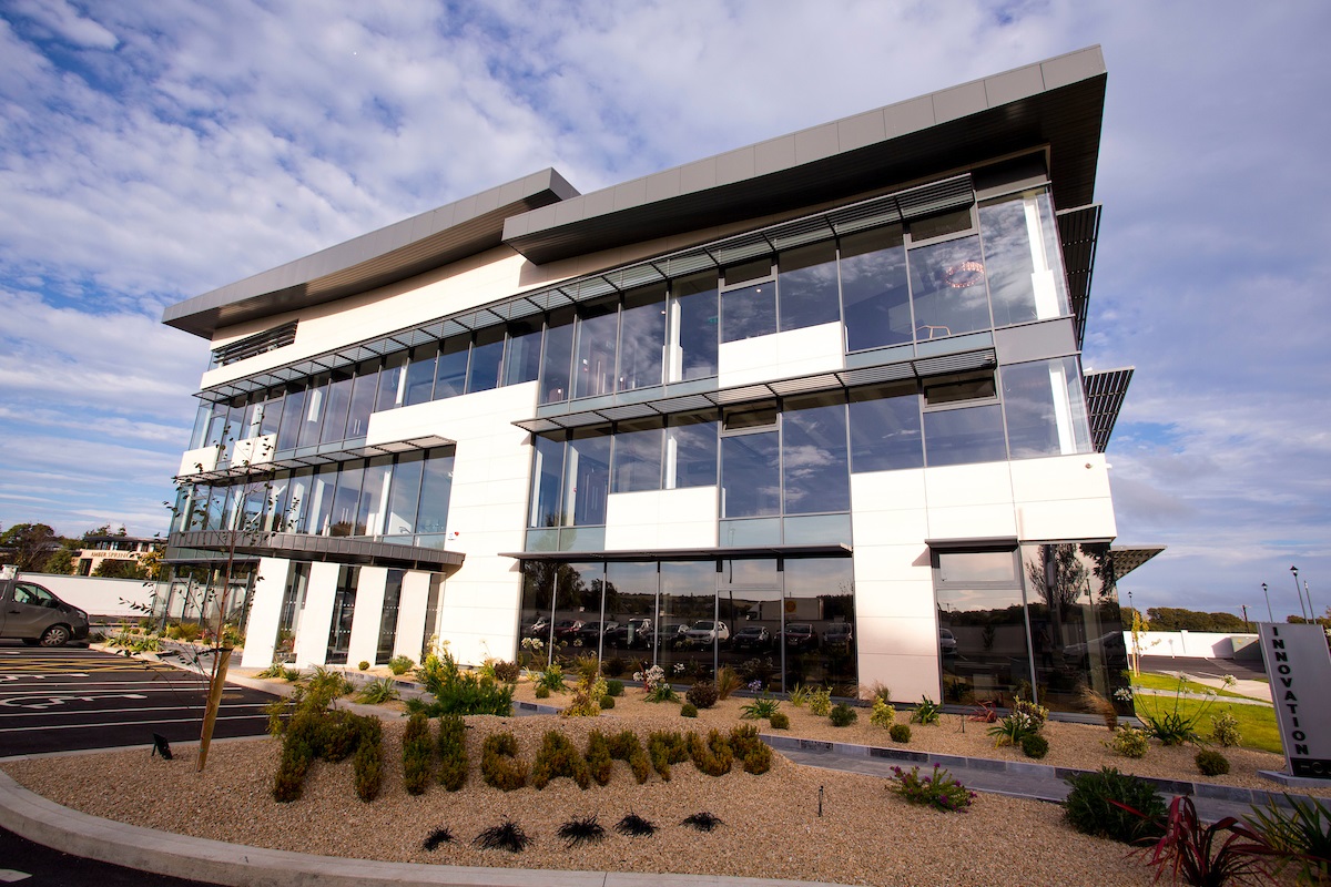 Exterior view of glass clad building that is M11 Business Campus in Gorey, Co. Wexford. It is a multi-storey, modern looking square building with fresh landscaping.