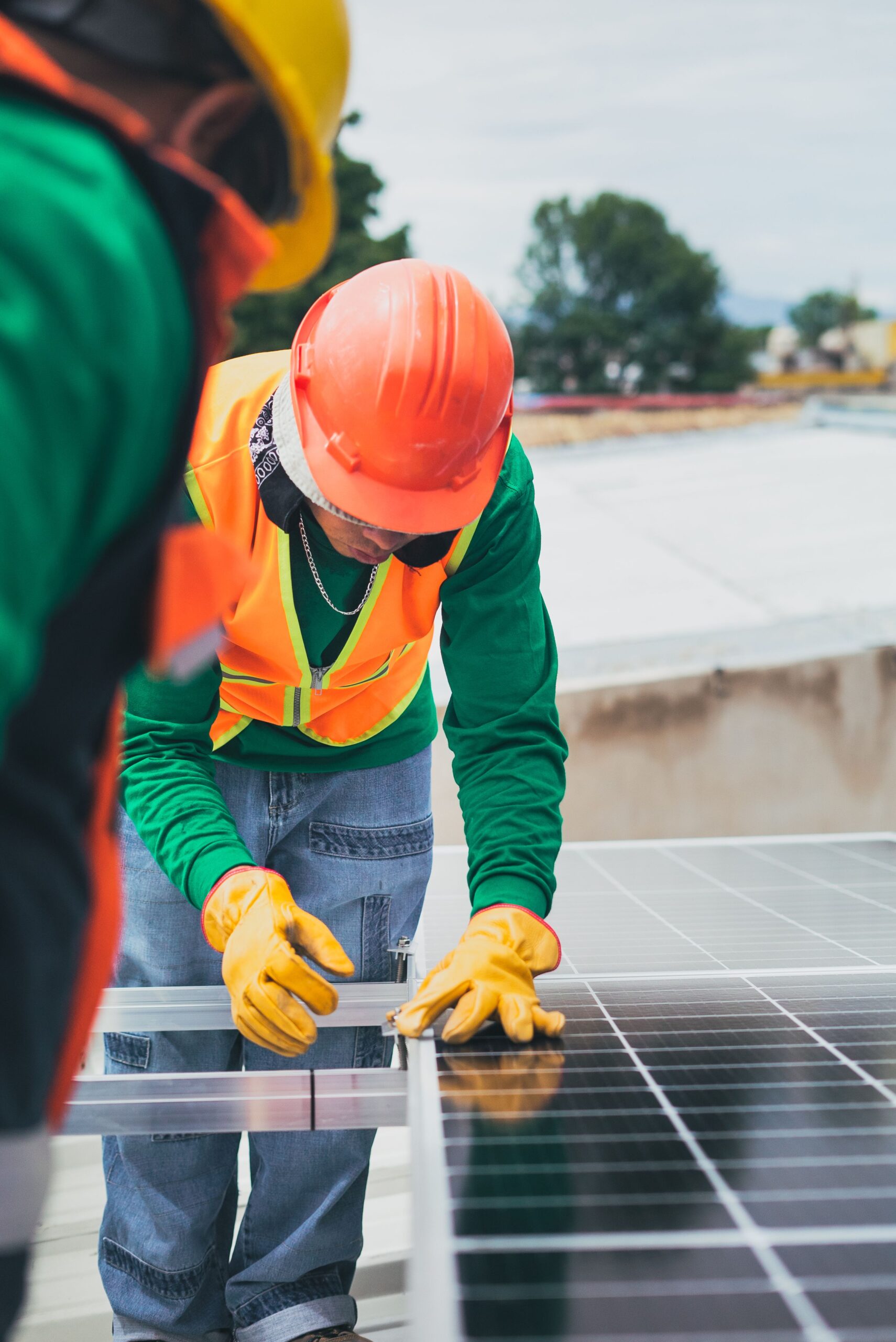 A solar power technician installing solar panels whilst wearing safety gear: a hi-vis and orange hard hat