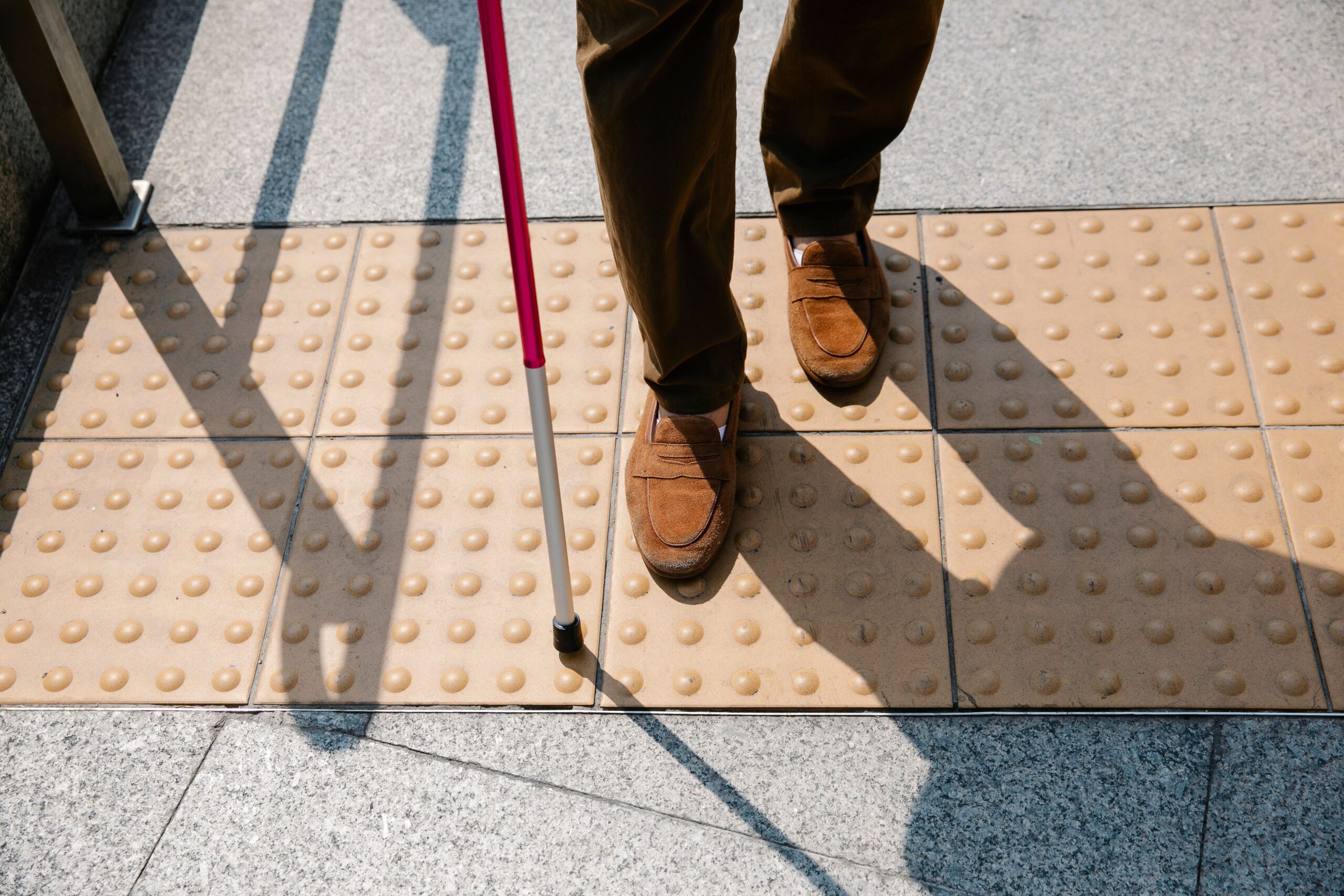 A person with a mobility cane standing on tactile strips at a crossing point