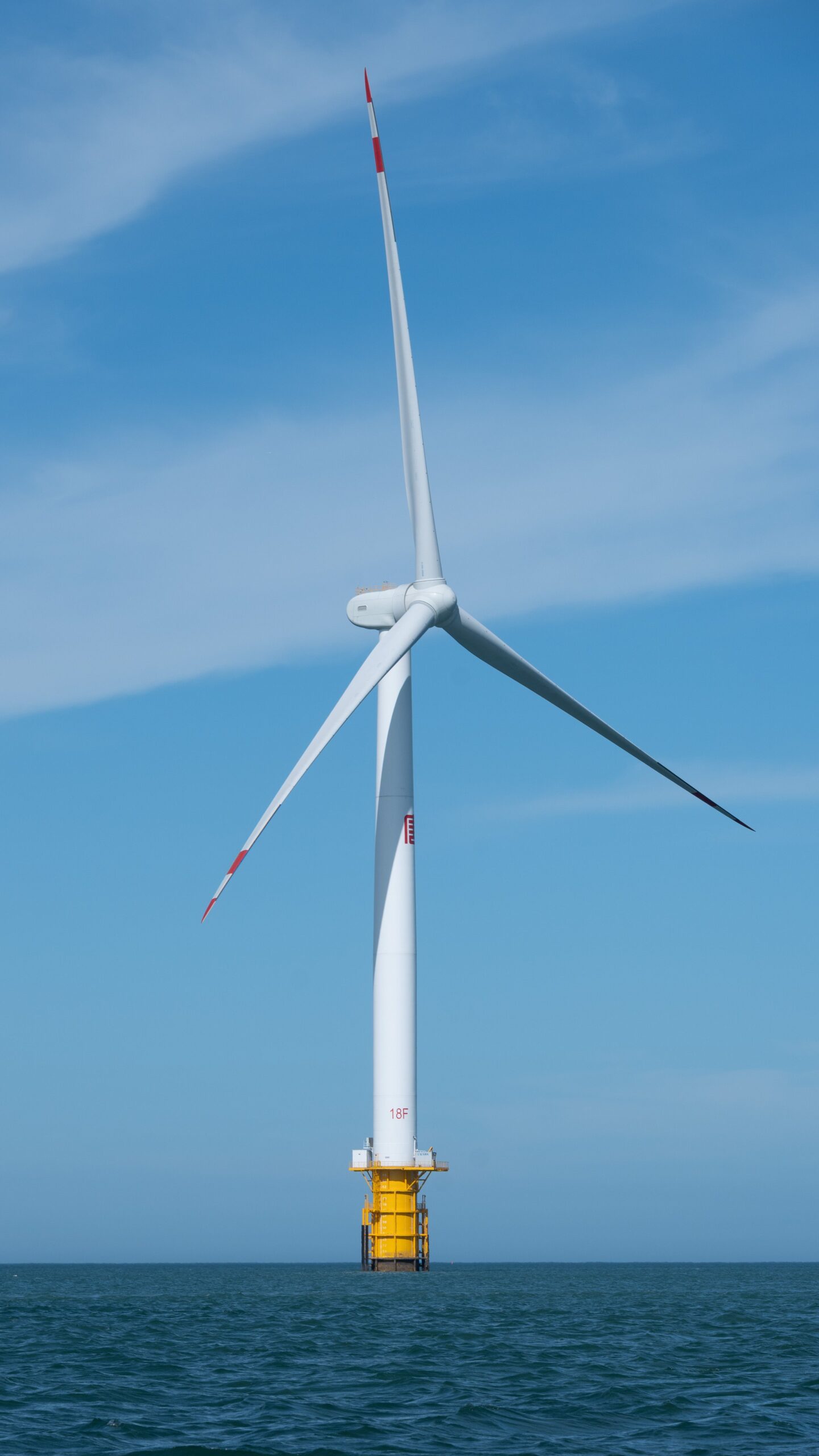 A solitary offshore wind turbine stands tall in the open sea under a bright blue sky