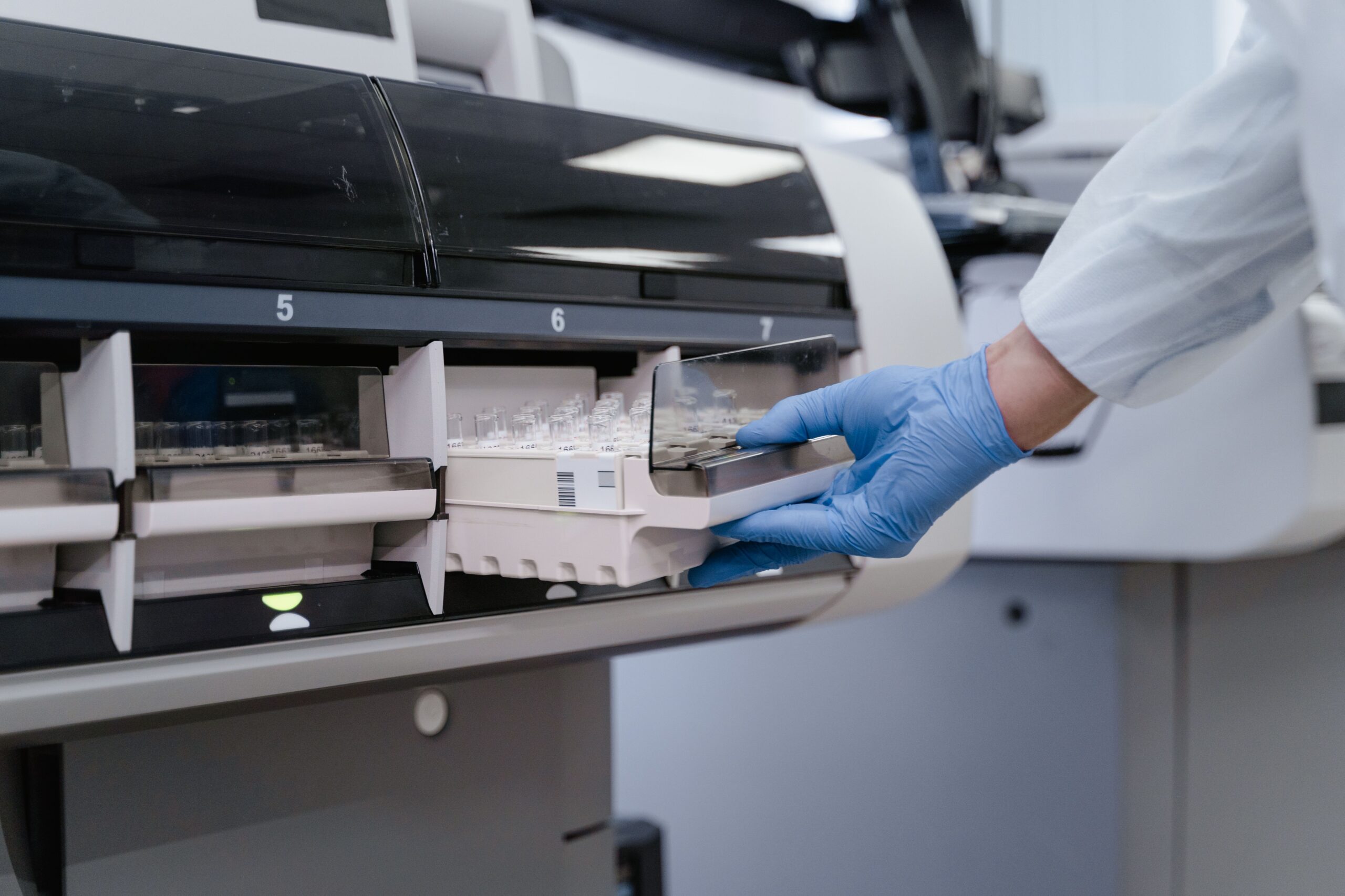A lab technician in blue gloves handling samples in a scientific instrument