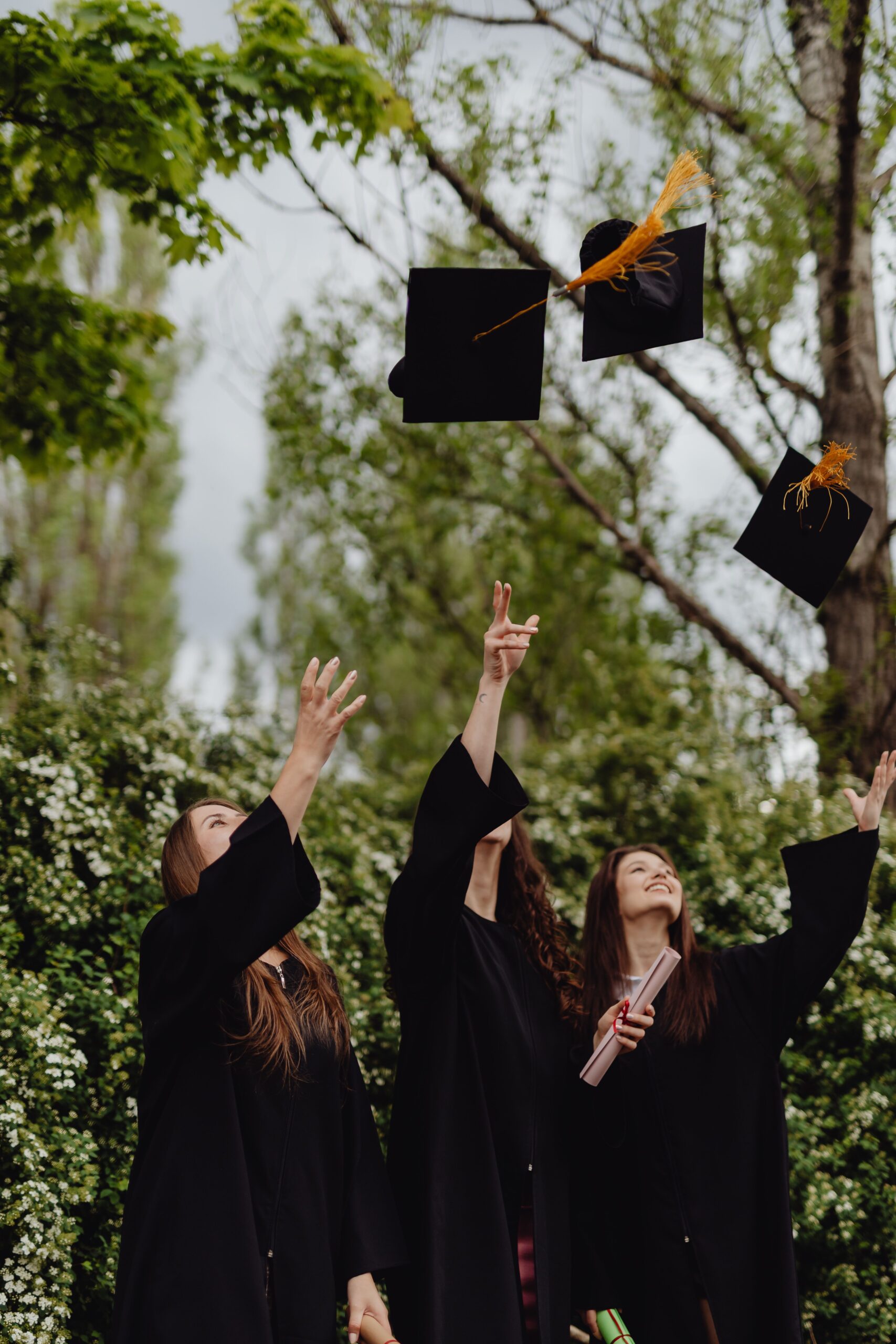Three women in black gowns throwing graduate black hats in the air