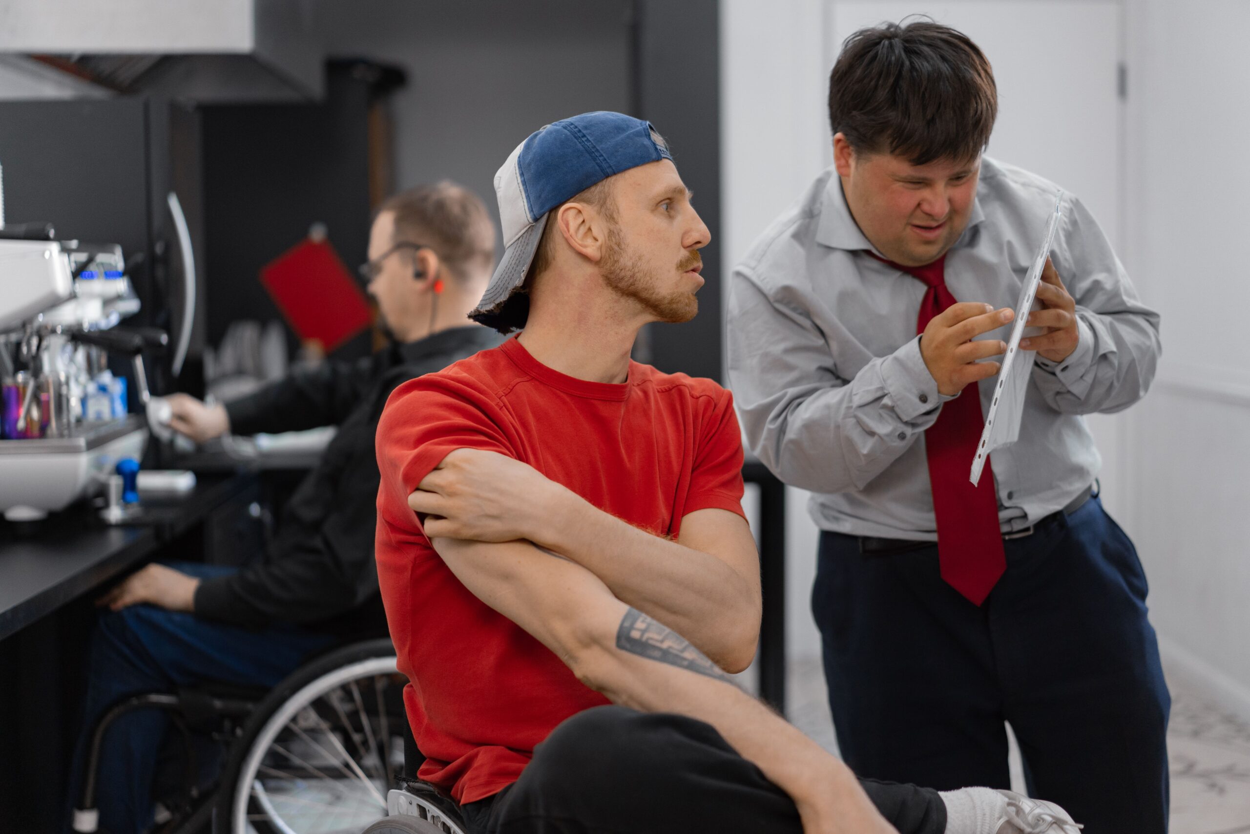 A wheelchair user helps a person with Down Syndrome with a task in an office environment